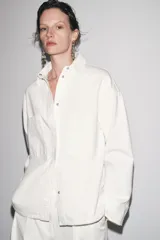 Sobrecamisa blanca de algodón con cuello solapa, manga larga y dos bolsillos de plastrón en el pecho. Cierre frontal con botones ocultos por solapa.