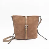 Cartera de gamuza color marrón con detalles de tachas metálicas en los laterales inferiores. Presenta una correa central vertical con hebilla decorativa en tono beige y correa larga ajustable para llevar al hombro o cruzada.