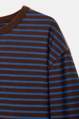 Camiseta de manga larga con diseño de rayas horizontales en color crudo y marrón oscuro. Presenta cuello redondo en contraste y corte regular con bajo recto.