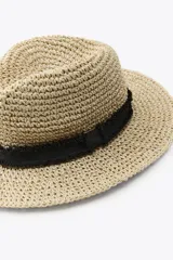 Sombrero de ala ancha tejido en paja color natural, con corona redonda y cinta decorativa negra de textura rugosa alrededor de la base de la corona.