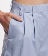 Short de sastrería confeccionado en tricolina de algodón, con diseño de tiro medio, pliegues delanteros, bolsillos laterales y bajo con dobladillo plegado. Cuenta con cierre de botón y cremallera, además de trabillas en la cintura.