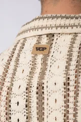 Camisa de manga corta tejida al crochet con diseño de rayas verticales negras sobre una base color crudo. Presenta cuello solapa y cierre frontal con botones.