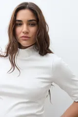 Remera de cuello alto tipo media polera, de manga corta y corte ajustado al cuerpo, en color crudo.