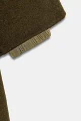 Parka oversize de corte recto confeccionada en tejido con mezcla de lana en color verde oliva. Presenta cuello alto con capucha, cierre frontal con botones y bolsillos laterales. Incluye detalles en tejido acolchado a contraste en la solapa frontal y puños.