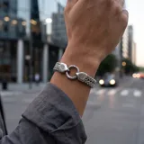 Pulsera de acero con diseño de cadena trenzada y cierre circular con detalles grabados.
