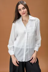 Camisa blanca de corte clásico con cuello camisero, manga larga y bolsillo frontal, que incluye una musculosa interior con detalle de encaje visible en el escote.