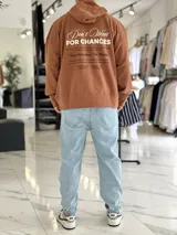 Canguro oversize color beige, con capucha y amplio estampado tipográfico en la espalda.