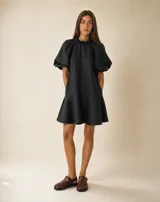 Vestido corto de lino negro con silueta amplia y relajada, cuello fruncido con volados y mangas abullonadas.