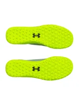 Championes de fútbol Under Armour Shadow Select 3 Turf, diseñados para césped artificial. Presentan un empeine sintético suave y resistente en color gris con detalles en amarillo neón, incluyendo el logo de la marca en negro. Cuentan con suela de goma con tacos multidireccionales para un agarre óptimo.