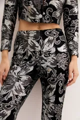 Pantalón de terciopelo negro con estampado floral en plateado, de corte acampanado.
