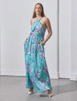 Vestido largo de gasa con estampado floral en tonos turquesa, rosa y verde. Tiene cuello halter cruzado, corte en la cintura con faja plisada y abertura en la espalda con cierre invisible.