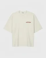 Camiseta color crema de algodón con cuello redondo y mangas cortas. Presenta un estampado pequeño con el logo de la marca en el frente.