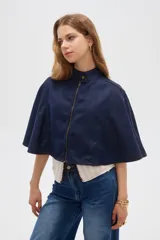 Poncho corto de denim azul con cuello alto, cierre frontal y diseño amplio de inspiración capa.