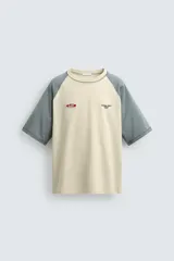Camiseta de corte relajado con mangas ranglán en color gris y cuerpo en color beige. Presenta cuello redondo, costuras a contraste y detalles de parches y bordados en el pecho.