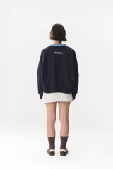 Buzo estilo rugby de corte oversized, color verde oscuro, con cuello tipo camisa en denim azul claro y cierre frontal parcial. Presenta un recorte horizontal en el pecho, logo bordado y tiras laterales en las mangas en contraste.