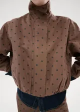 Chaqueta bomber de algodón color marrón con estampado de lunares, cuello embudo, manga larga, bolsillos laterales y cierre oculto con cremallera y botones a presión.