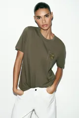 Camiseta de algodón con efecto lavado, cuello redondo y manga corta. Presenta un detalle de fornitura metálica aplicada en el pecho.