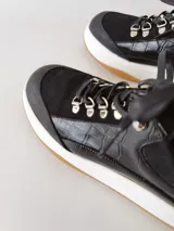 Zapatillas deportivas negras de cuero, con cordones y suela de goma blanca con base marrón.