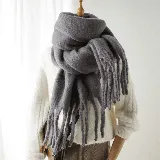 Bufanda de tejido de punto grueso y suave, color gris, con diseño de flecos largos en los extremos.