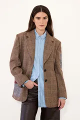 Blazer de corte sastrero confeccionado en paño con estampado de cuadros escoceses. Presenta parches decorativos en las mangas y espalda, bordados en el bolsillo y manga, y cierre frontal con botones.