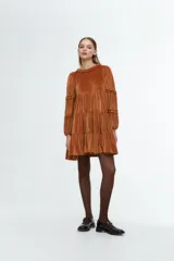 Vestido corto de terciopelo color tostado, con diseño de tres niveles con volados, cuello redondo con detalle de fruncido y mangas largas con volados aplicados.