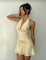 Vestido corto amarillo claro con estampado de rayas diagonales, escote halter y drapeado en el busto. La falda es acampanada y tiene detalles fruncidos en la cintura.