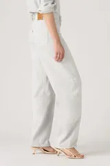 Pantalón de jean estilo baggy con corte barrel, tiro alto y pierna ancha. Presenta un tono gris claro lavado, con costuras reforzadas y diseño de cinco bolsillos.