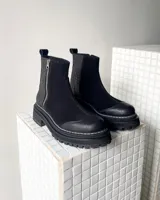 Botas cortas de cuero vacuno color negro, con diseño combinado de gamuza y cuero texturizado con efecto reptil en el talón. Presentan cierre lateral metálico, puntera reforzada y suela track dentada con costura visible.