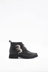 Botín de cuero vacuno color negro, con diseño de estilo western que presenta dos correas laterales con hebillas metálicas decorativas y detalle de tachas metálicas en la puntera.