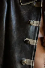 Campera estilo militar napoleón confeccionada en cuero ovino, con cierre frontal y solapa decorativa con botones metálicos y alamares de gamuza en tono crudo. Cuenta con cuello camisero, pespuntes visibles y diseño estructurado de manga larga.