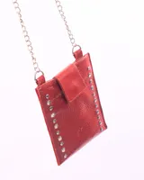 Bolso porta celular de cuero rojo con acabado texturizado, decorado con remaches metálicos plateados en los laterales. Cuenta con una solapa de cierre y una correa de cadena metálica.