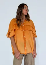 Camisa amarilla con cuello mao, mangas cortas y volados en el pecho.