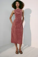 Vestido midi de piel color rosado, con cuello redondo y diseño sin mangas. Presenta costuras marcadas y cierre en la espalda con cremallera oculta.