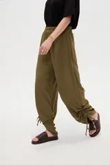 Pantalón verde militar de corte ancho y tiro alto, con cintura elástica fruncida y detalles de cordones ajustables en los tobillos.