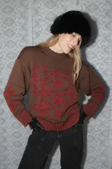 Buzo de tejido de punto grueso color marrón con diseño geométrico y floral estampado en color rojo. Presenta cuello redondo, mangas largas y puños y ruedo acanalados.
