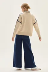 Sweater de tejido de punto color beige, con cuello redondo y detalles de bordado en zigzag en color azul oscuro a lo largo de las mangas y hombros. Presenta un pequeño bordado con texto en el pecho.