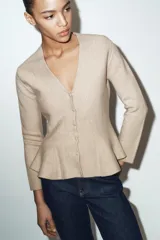 Chaqueta entallada de punto con escote en pico y manga larga. Presenta un diseño con bajo en evasé tipo peplum y cierre frontal con botones forrados a tono.