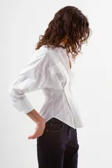 Camisa azul de algodón con finas rayas blancas verticales, cuello mao, manga larga y detalle de pinzas y botones en la zona de la cintura. Posee dos bolsillos de parche con tapa en el pecho.