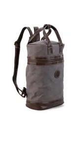 Mochila matera de diseño vertical, confeccionada en tela canvas marrón con detalles y refuerzos en cuero sintético oscuro. Cuenta con doble asa superior de mano, correas traseras regulables, cierre metálico frontal y bolsillo posterior.