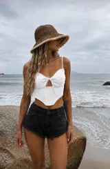 Top blanco estilo corset con tirantes finos, escote pronunciado con detalle de lazo frontal y abertura tipo gota, con diseño en pico en el dobladillo inferior.