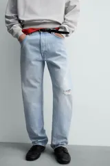 Jeans de denim de algodón, tiro medio, color celeste claro lavado. Corte recto y holgado desde la cadera hasta el tobillo, con rotura en una de las perneras. Presenta cierre frontal con cremallera y botón, y cinco bolsillos.