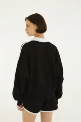 Buzo negro de felpa con cuello polo y solapa blanca, mangas largas con franjas blancas en los laterales y estampado en el pecho con la palabra "RIO" y detalles gráficos.