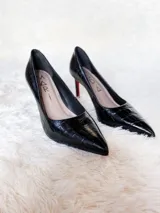 Zapatos de tacón alto con textura de reptil, color negro, con suela roja característica.
