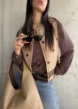 Chaleco de gamuza beige con bordados étnicos, detalles de tachas metálicas en los bordes y cierre abierto.