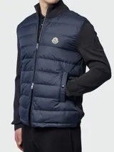Campera híbrida Moncler con frente acolchado en color azul marino y mangas de tejido de punto en color negro. Presenta cuello alto tejido, cierre frontal completo y bolsillos laterales con cierre. Incluye el logo de la marca en el pecho y en la manga.