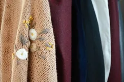 Saco de tejido de punto color tostado, con bordados artesanales de flores y hojas en la manga. Diseño envolvente y cómodo.