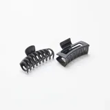 Pack de dos pinzas para el pelo, una con forma de espiral y otra rectangular con diseño calado, ambas de color negro.