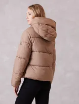 Campera puffer de corte recto y acabado mate, con diseño de bloques horizontales acolchados. Presenta capucha integrada con cordones de ajuste, cierre frontal metálico y bolsillos laterales invisibles. Incluye puños elásticos internos para mayor protección contra el frío.