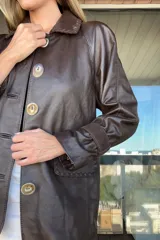 Tapado de cuero ovino color chocolate con detalles de pasamanería y presillas en gamuza al tono. Presenta cierre frontal con botones grandes y mangas largas con puños ajustados.