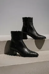 Bota corta de cuero color suela, con taco cuadrado y punta fina. Presenta costuras verticales decorativas en el empeine y cierre lateral.